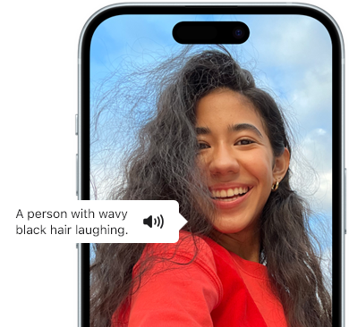 Un iPhone 15 montrant la fonctionnalité VoiceOver énonçant les informations figurant sur l’image : Une personne aux cheveux noirs ondulés en train de rire