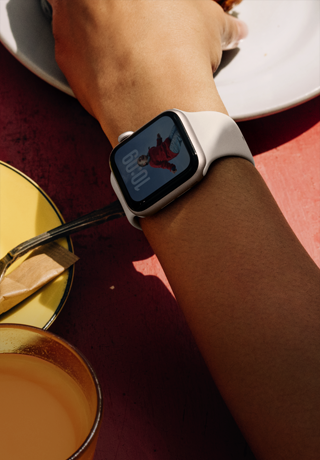 Une personne prend son petit-déjeuner, Apple Watch SE 3 au poignet, boîtier en aluminium lumière stellaire, écran toujours activé, cadran affichant le portrait d’une personne, Bracelet Sport lumière stellaire